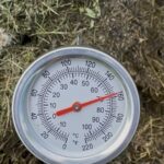 Kompostový teploměr v hromadě trávy ukazuje 70 °C, teplotu která ničí semena plevele